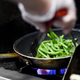 A cook in a restaurant kitchen sauteing green beans in a pan on the stove